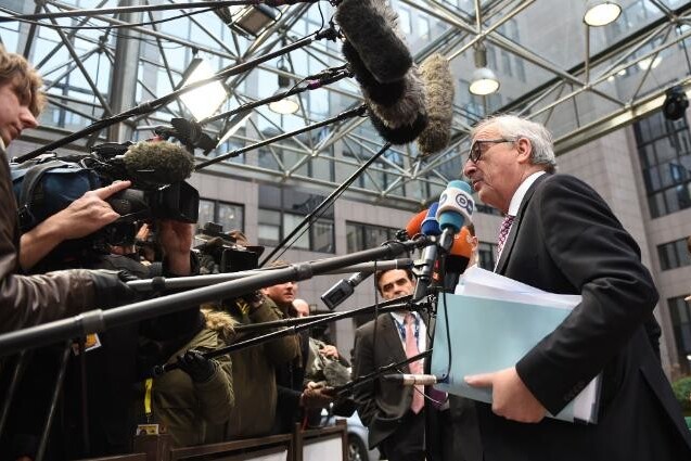 An interview taking place with press surrounding a man with microphones