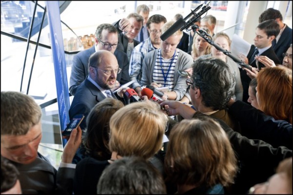 A photo showing a man surrounded by journalists holding microphones to him
