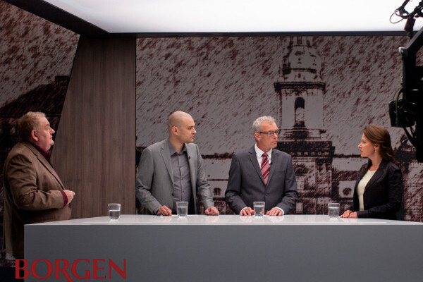 A panel of four people stand at a desk having a discussion