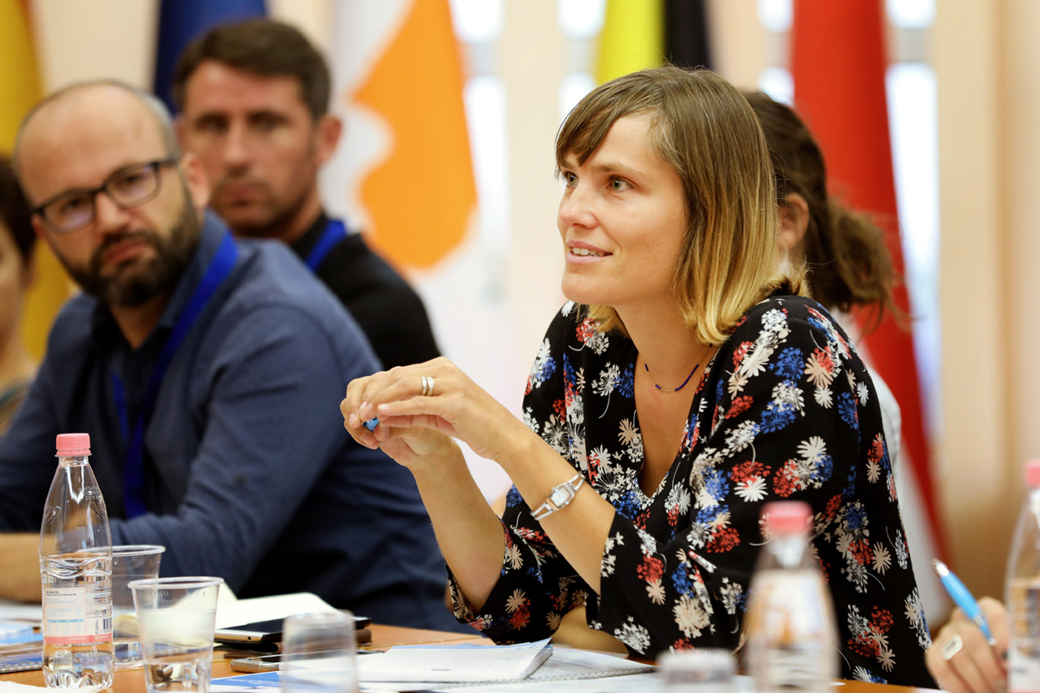 A woman engages with others at an EU event - sitting around a table with flags in the background