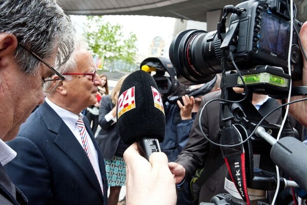 A photo showing a man surrounded by journalists holding microphones to him