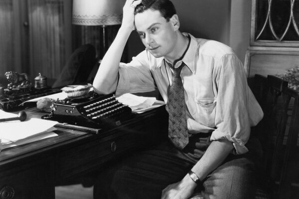 A troubled writer sits at a typewriter looking frustrated