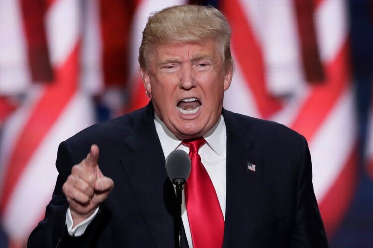 President Donald Trump giving a speech with American flags flying behind him